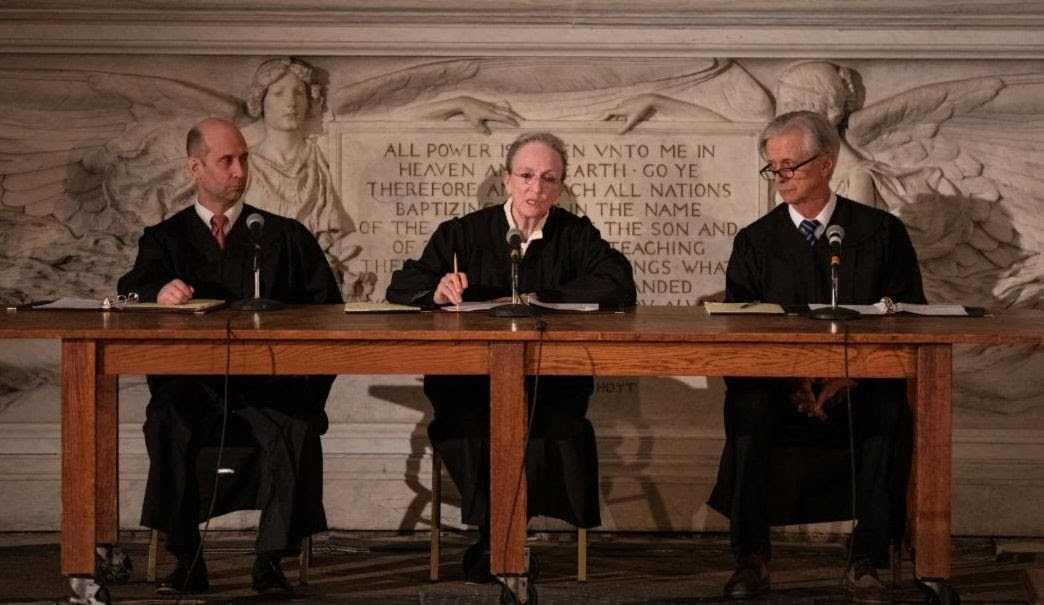 Kathleen Chalfant (center) in a scene from Waterwell's production of "The Courtroom: A Re-Enactment of Deportation Proceedings". 